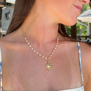 Woman wearing a gold necklace with a sun pendant outdoors
